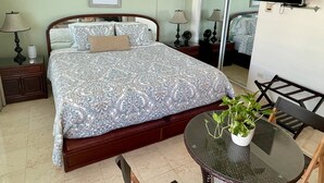 A bedroom with a bed, bedside lamps, a TV, a mirror, and a small table with a plant. - Luxurious Ocean View Studio Next to Major Hotels (Carolina)