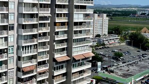 A high-rise building with multiple balconies, a parking lot, and a view of a green landscape in the background. - Luxurious Ocean View Studio Next to Major Hotels (Carolina)