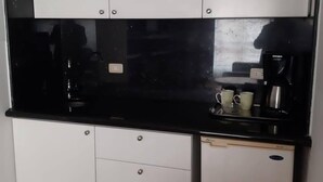 Una cucina compatta con mobili bianchi, un piano di lavoro nero e una macchina da caffè.