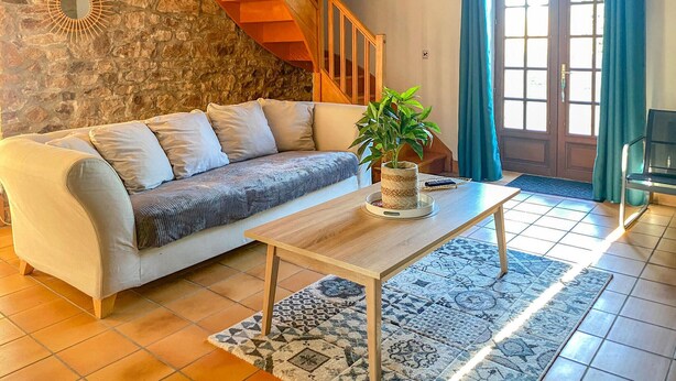 A living room with a sofa, a coffee table, a potted plant, a stone wall, a wooden staircase, and a view through a door with curtains. - Gorgeous home in St. Pierre Langers (St. Pierre Langers)