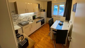 A compact kitchen with a marble backsplash, a dining area with a table and chairs, and a window with a view of buildings outside.