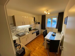 A compact kitchen with a marble backsplash, a dining area with a table and chairs, and a window with a view of buildings outside.
