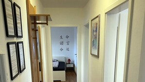A hallway with wooden flooring, a bed with a red lamp, and a door with a keypad lock.