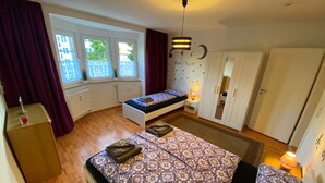 A bedroom with two beds, a wardrobe, a bedside table with a lamp, and a window with curtains.