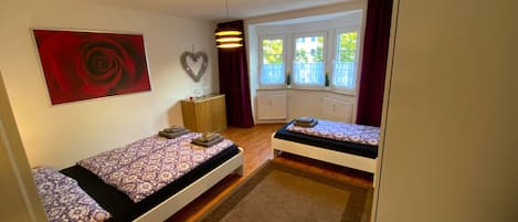 Una habitación pequeña y luminosa con dos camas, una decoración con forma de corazón y una ventana que da a vistas de vegetación.