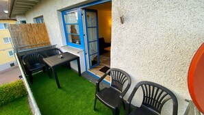 An outdoor patio with a table and chairs, a blue-framed door, and a small window with lace curtains.