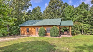 A log cabin with a green roof, a porch with chairs, and a well-maintained lawn.