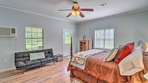 A bedroom with a bed, a ceiling fan, a window, a door, and a couch.