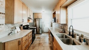 A modern kitchen with wooden cabinets, stainless steel appliances, and a large window providing natural light. - CITY COTTAGE, CITY COTTAGE GETWAY, FENCE BACKYARD (Saint Paul)
