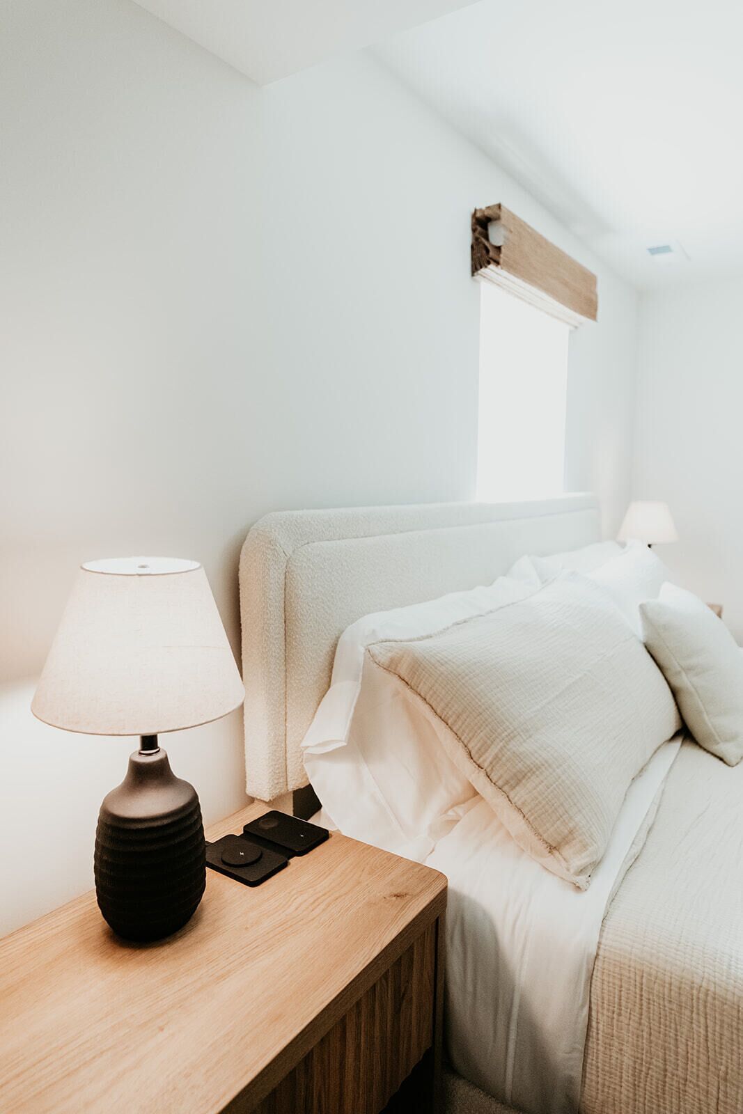 Een keurig opgemaakte slaapkamer met een houten nachtkastje, een lamp en een bed met witte beddengoed.