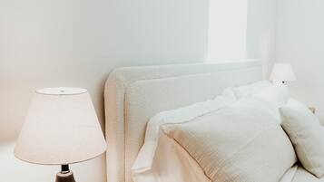 Een keurig opgemaakte slaapkamer met een houten nachtkastje, een lamp en een bed met witte beddengoed.