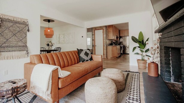 A modern living room with a leather sofa, a fireplace, and a kitchen in the background. - CITY COTTAGE, CITY COTTAGE GETWAY, FENCE BACKYARD (Saint Paul)