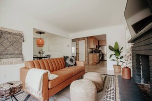 A modern living room with a leather sofa, a fireplace, and a kitchen in the background. - CITY COTTAGE, CITY COTTAGE GETWAY, FENCE BACKYARD (Saint Paul)