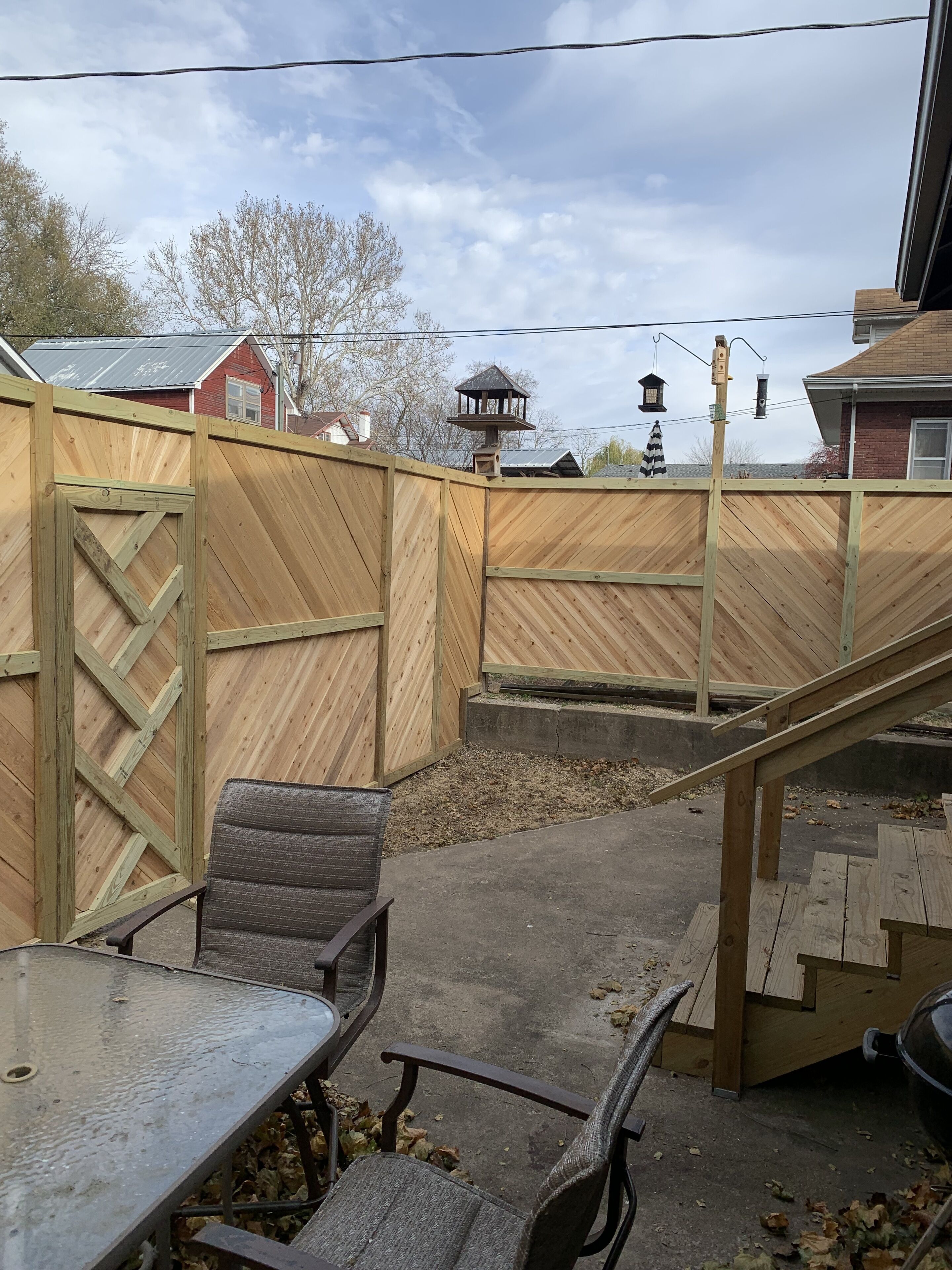 A backyard with a wooden fence, a patio table, chairs, and a bird feeder.