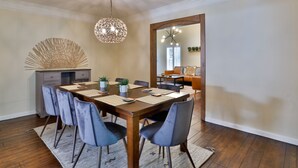 A dining area with a wooden table, blue chairs, a woven light fixture, and a mirror reflecting a window and a sofa. - City Paradise: Saltwater Pool/Spa (Los Angeles)