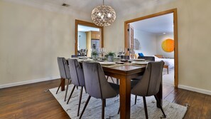 A dining area with a wooden table set for six, surrounded by six chairs, and a hanging light fixture above.