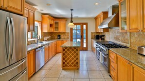 A kitchen with wooden cabinets, a stainless steel refrigerator, a granite countertop, and a central island. - City Paradise: Saltwater Pool/Spa (Los Angeles)