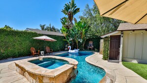 A swimming pool with a hot tub, surrounded by stone tiles, and a covered patio area with chairs and umbrellas. - City Paradise: Saltwater Pool/Spa (Los Angeles)