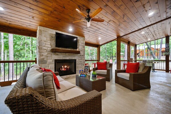 A covered outdoor seating area with wicker furniture, a stone fireplace, and a television. - NEW!! Escape to Modern Luxury in Broken Bow, Oklahoma! Blissful Pines Sleeps 14! (broken bow)