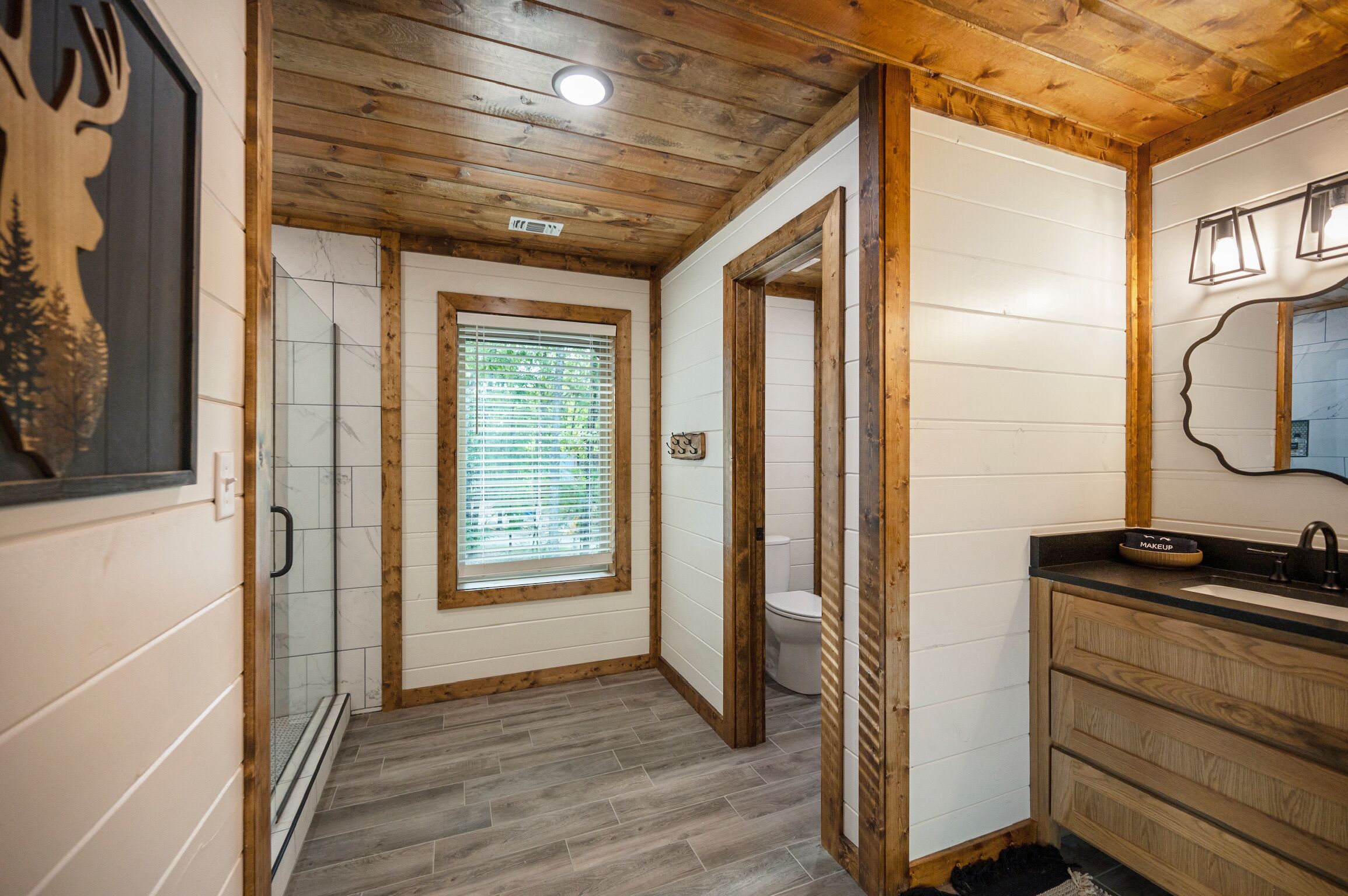 A wooden-paneled bathroom with a toilet, sink, and shower.