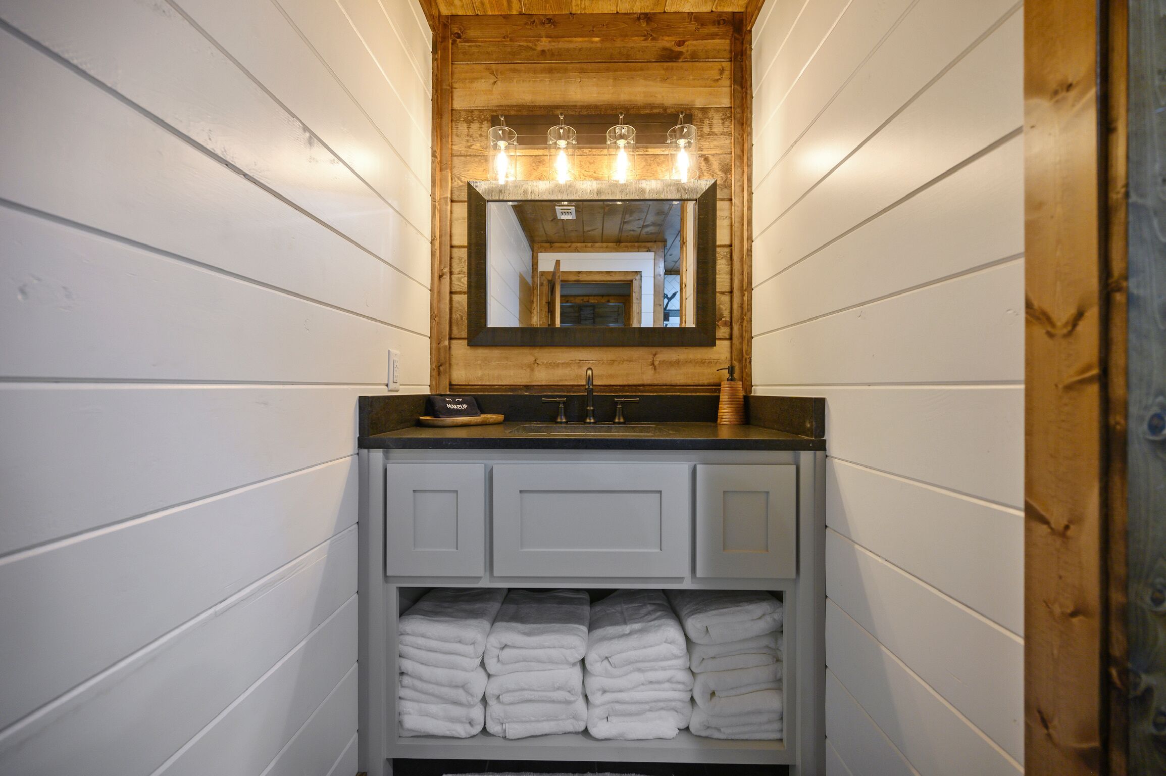 Un baño con techo de madera, espejo con iluminación, lavabo y toallero.