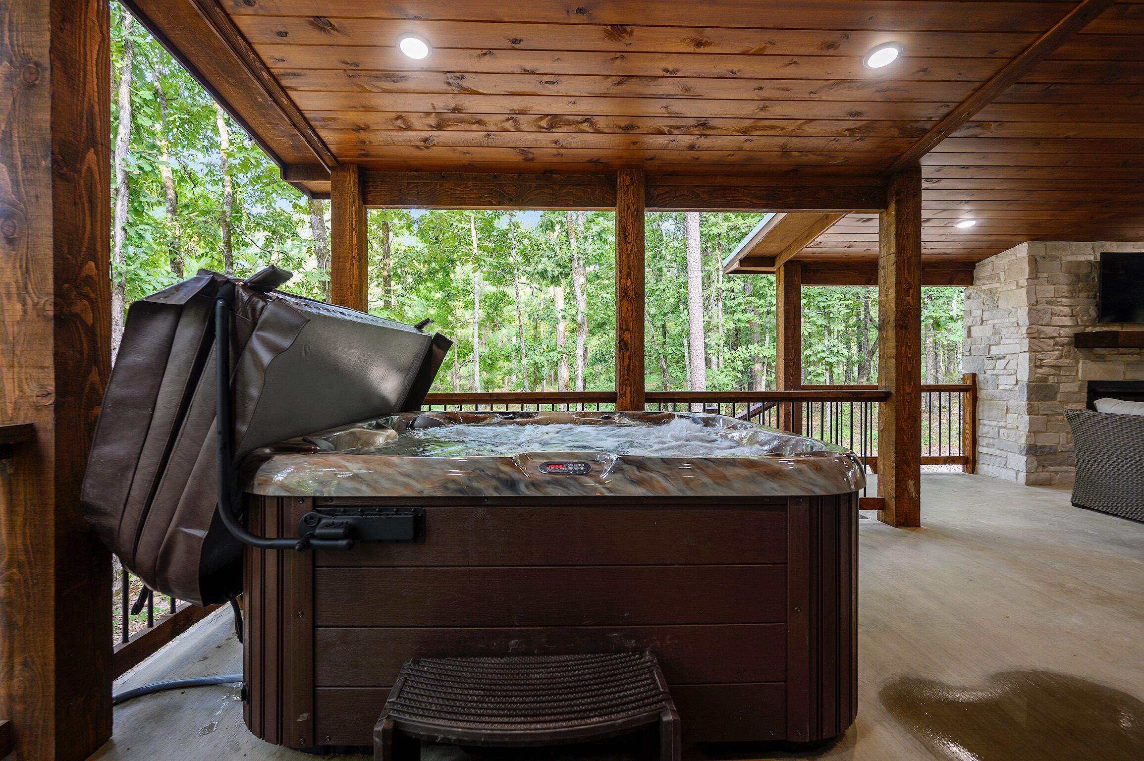 Un jacuzzi con asiento, chimenea de piedra y vista al bosque.