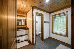 A wooden-paneled bathroom with a sink, mirror, and toilet. - NEW!! Escape to Modern Luxury in Broken Bow, Oklahoma! Blissful Pines Sleeps 14! (broken bow)
