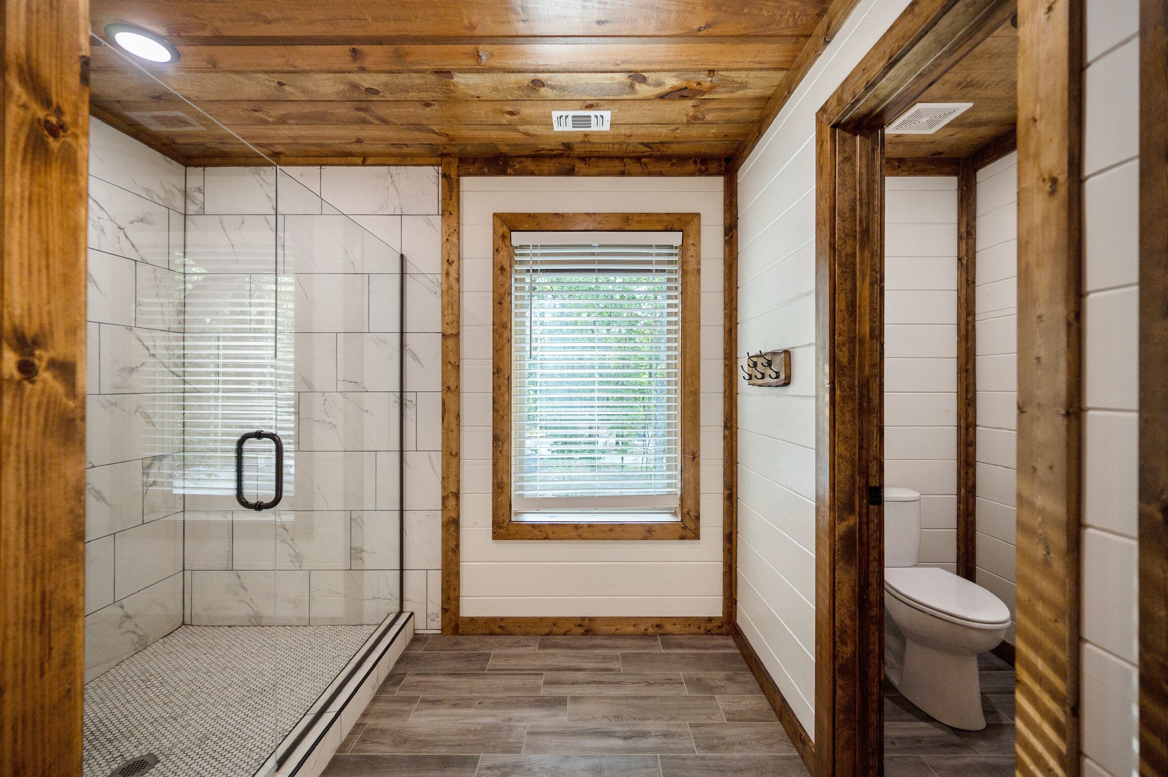 Un baño con ducha, inodoro y una ventana con persianas.