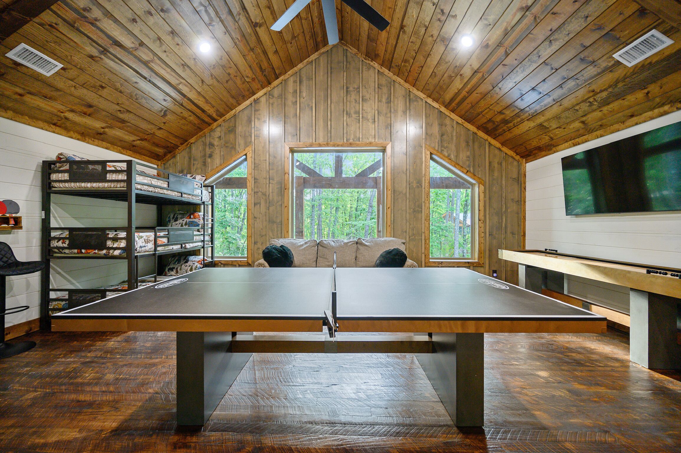 Una mesa de ping pong en una habitación con paredes de madera y techo inclinado.