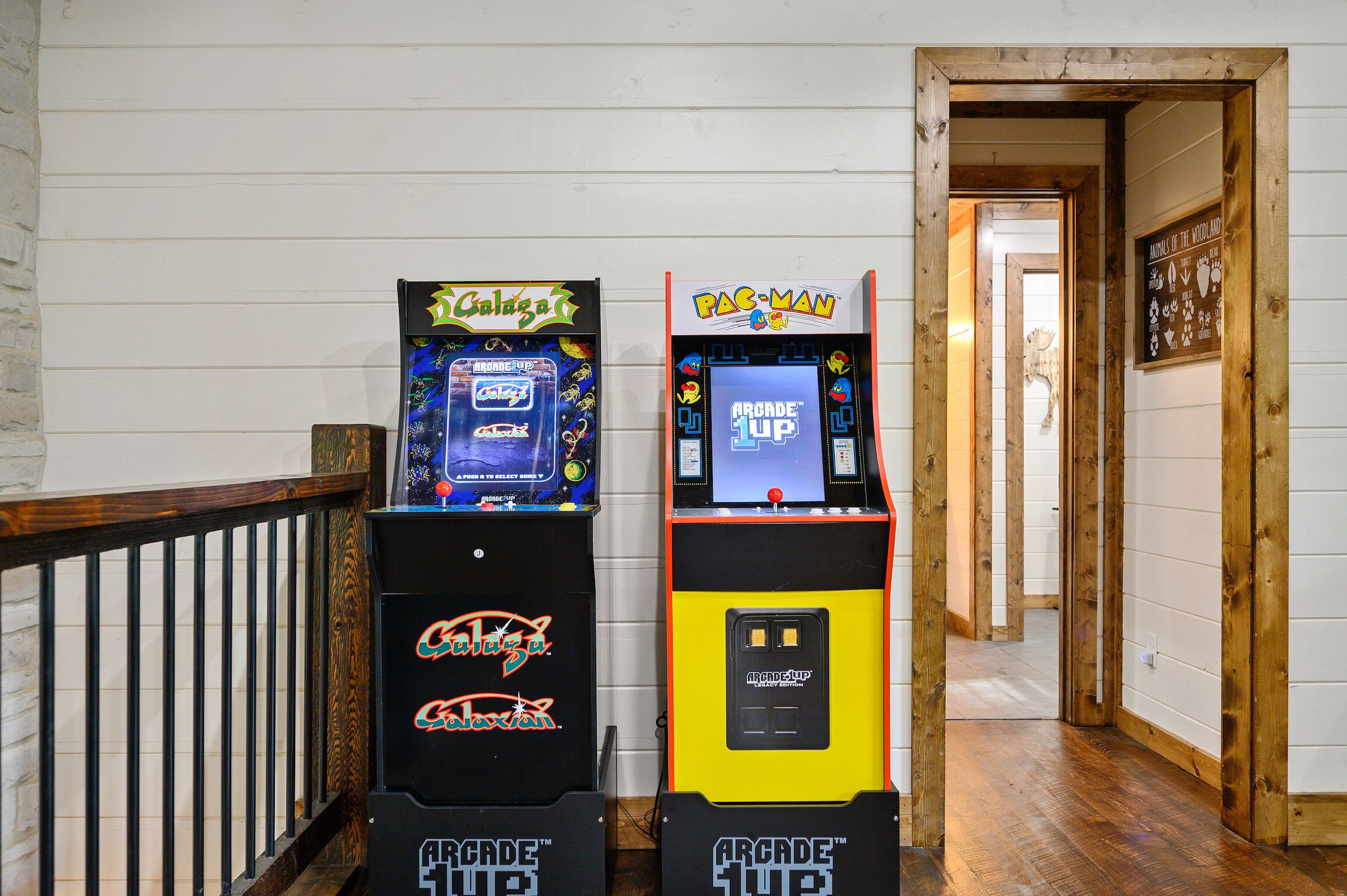 Zwei Spielautomaten, einer mit der Aufschrift 'Caligula' und der andere 'Pac-Man', in einem Korridor mit Holzwänden und einer Geländer.