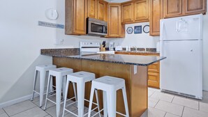 Een keuken met houten kastjes, een magnetron, een koelkast, een fornuis en barstoelen.