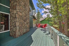 A wooden deck with a stone wall, outdoor furniture, and a view of a green house in the background. - Deck + Yard: Family-Friendly Pinetop Retreat (Pinetop)