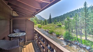 Une terrasse en bois avec une table et des chaises, offrant une vue sur une rivière et des montagnes boisées.