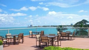 An outdoor patio with tables and chairs, overlooking a body of water and a cityscape. - Marlene's Executive Beachfront Condo (Nueva Gorgona)