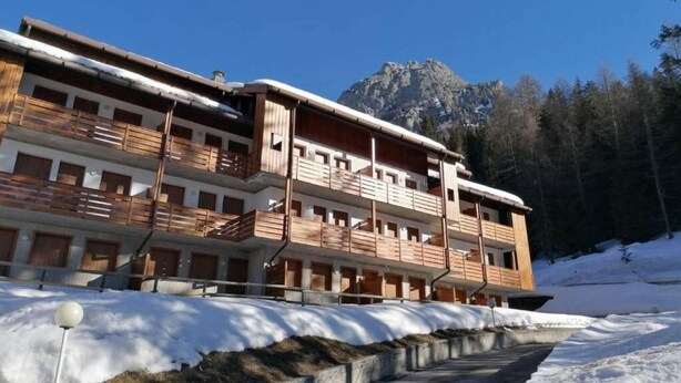 Un immeuble à plusieurs étages doté de balcons, un sol recouvert de neige et une montagne en arrière-plan.
