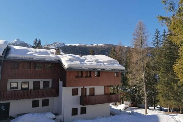 A two-story building with a wooden facade and balconies, surrounded by snow and trees.