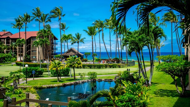A resort with a pool, palm trees, and a view of the ocean. - Sunny corner unit, natural light and breezy vibes (Lahaina)