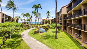 A resort with a pool, palm trees, and a view of the ocean. - Sunny corner unit, natural light and breezy vibes (Lahaina)