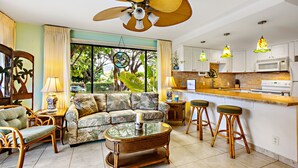 A living room with a sofa, chairs, a coffee table, and a kitchen area with a bar. - Sunny corner unit, natural light and breezy vibes (Lahaina)