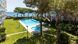A pool area with a view of the sea, surrounded by trees and a building with balconies.