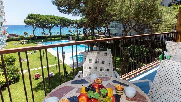 A balcony with a table set for breakfast, overlooking a pool and a view of the sea.