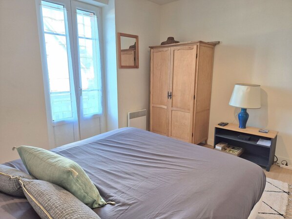 A bedroom with a bed, a wardrobe, a nightstand with a lamp, and a window with curtains.