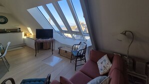 Ein Loft-Wohnraum mit Dachfenster, einer Küchenzeile und einer Sitzecke inklusive Sofa und Sesseln.