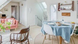 Ein modernes Wohnzimmer mit Essbereich, inklusive Treppe, einem rosa Sofa und einem Tisch für zwei Personen.