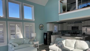 A spacious living room with a high ceiling, a kitchen with modern appliances, and a dining area. - Peaceful Waterfront Family Retreat in North Ocean City (Ocean City)