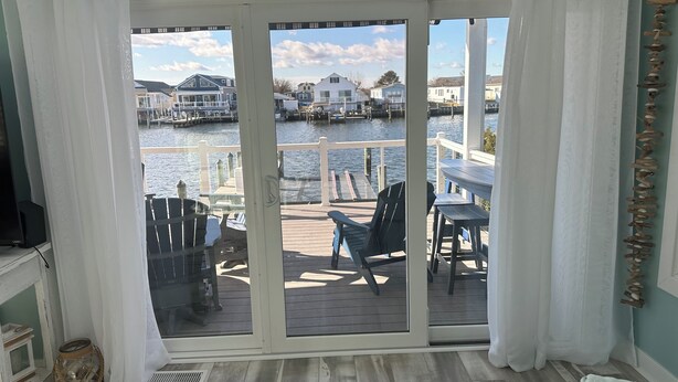 A room with a view of a dock and water, featuring a sliding glass door, a table with chairs, and a small speaker. - Peaceful Waterfront Family Retreat in North Ocean City (Ocean City)