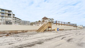 Un hotel frente a la playa con una playa de arena, una escalera de madera y un edificio con varios balcones.