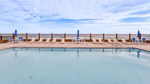 Una piscina con sillas de descanso y sombrillas, una valla de madera y vista a la playa.