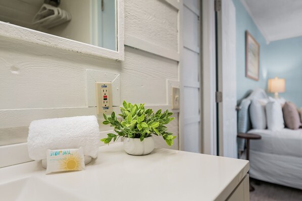 A bathroom with a white countertop, a towel, a potted plant, and a wall-mounted power outlet.