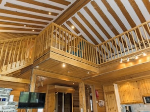 Ein Holzinterieur mit Balkon, Flachbildfernseher und Küchenzeile.